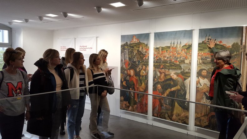 Man sieht viele junge Menschen bei einer Museumsführung. Die Führer*innen beschreibt ein Bild. 